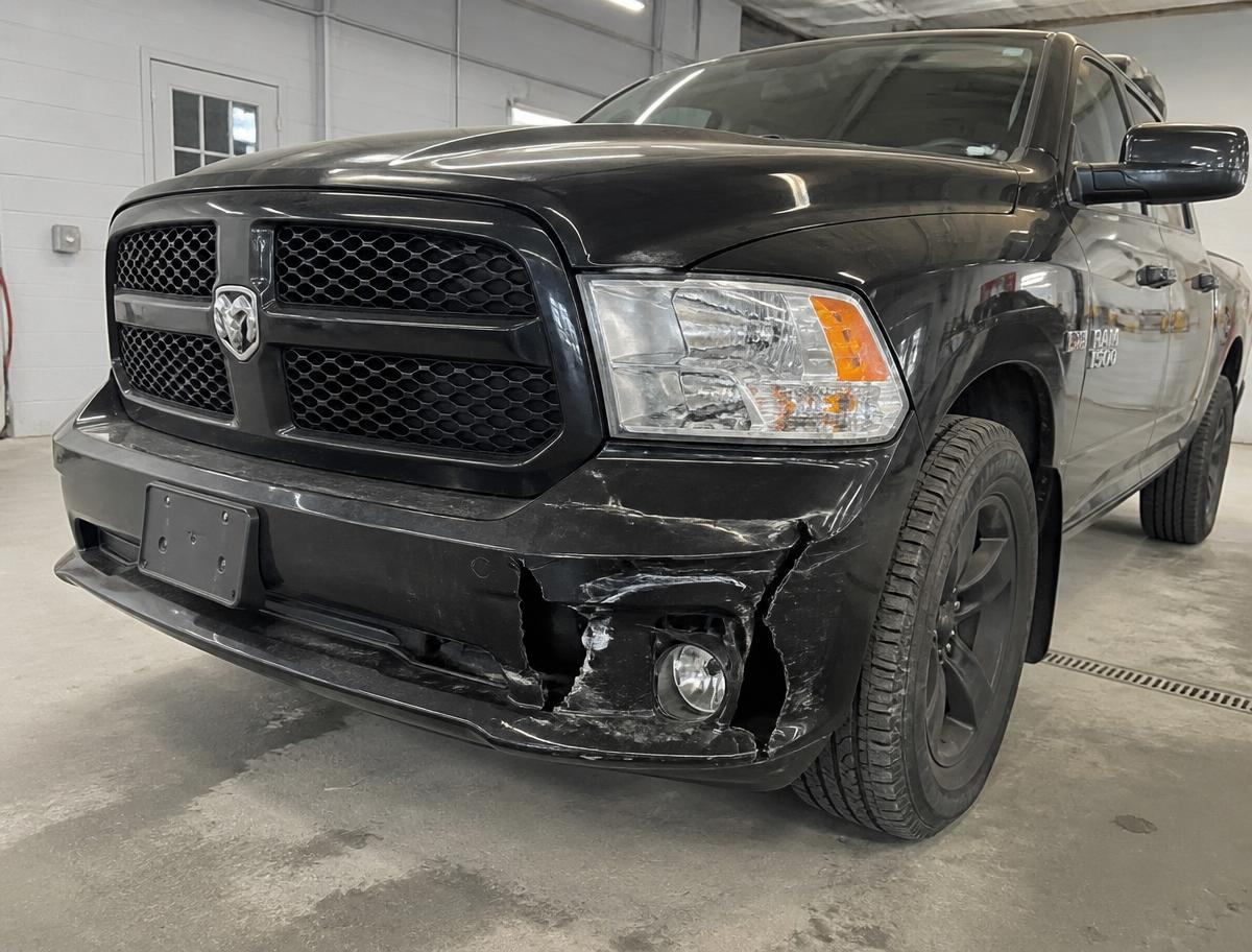 Black pickup truck front bumper cracked and torn with a damaged fog light before repair