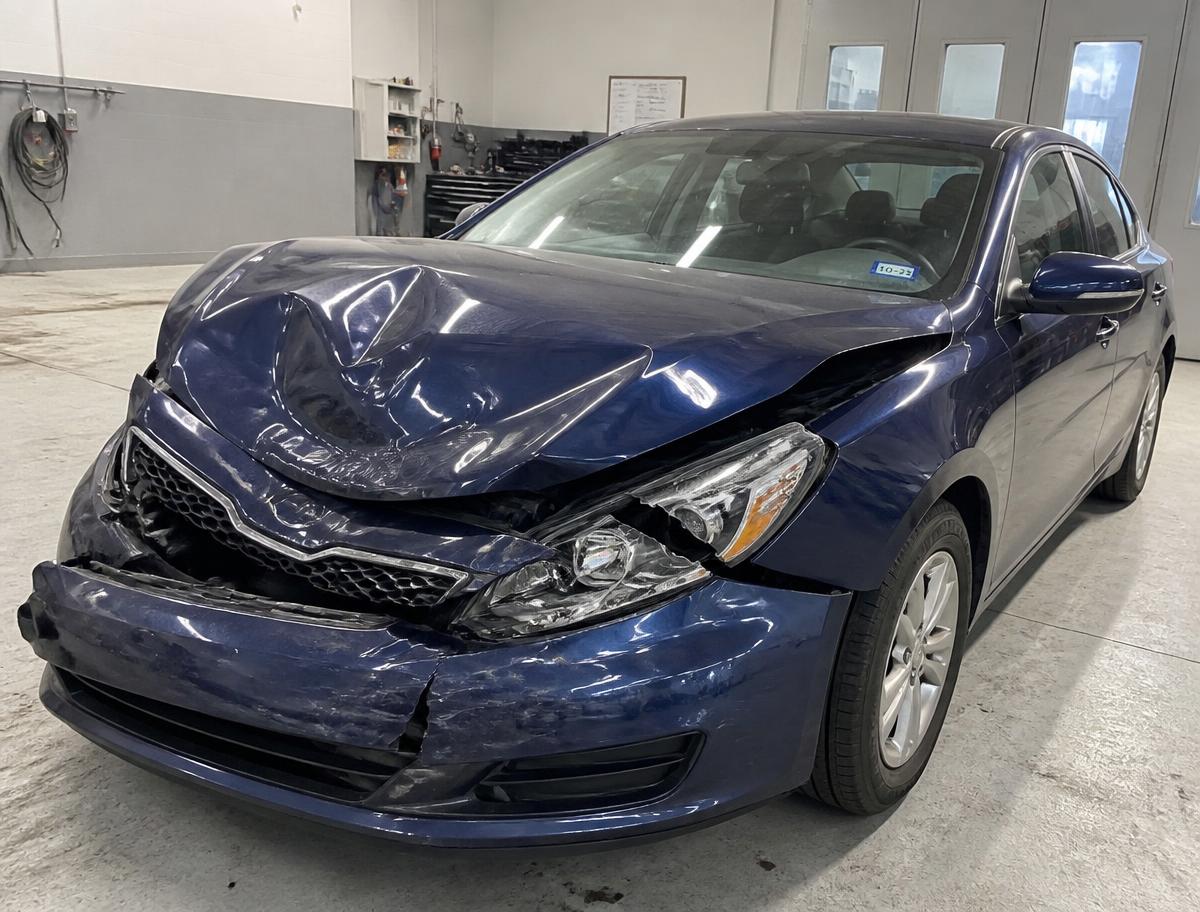 Dark blue sedan with a crumpled hood, pushed in bumper and broken headlight before accident repair