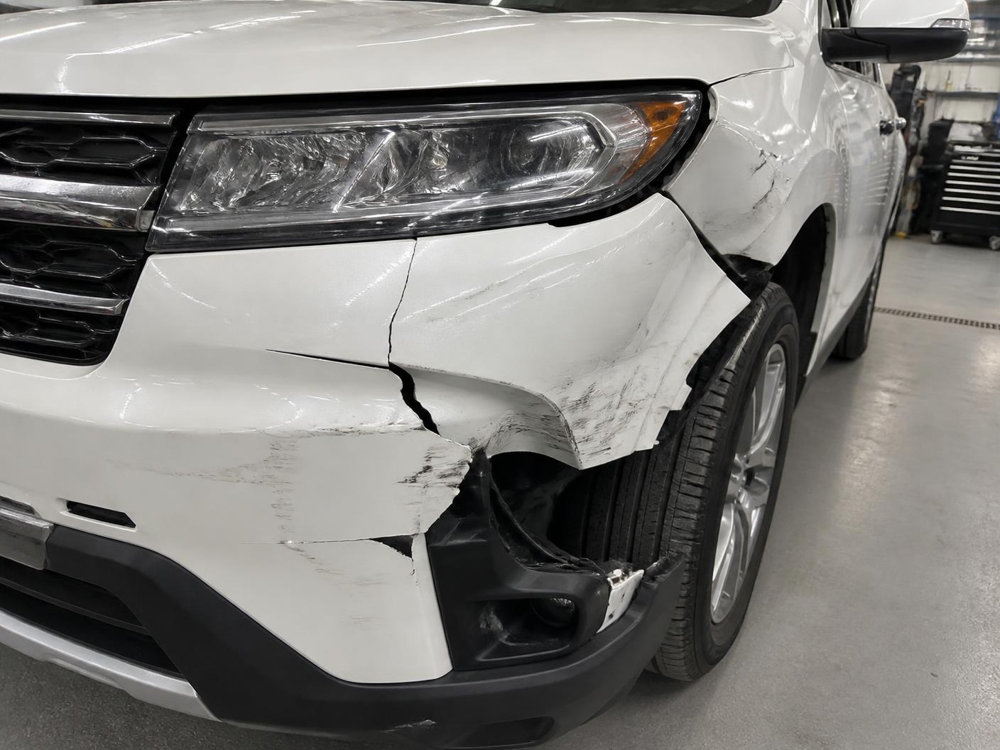 White SUV front bumper cracked and torn with a pushed-in fender before repair