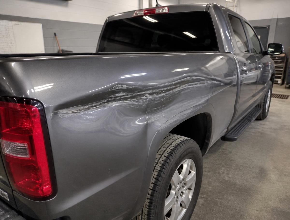 Gray pickup truck bed side with a long dent and deep scrape before body shop repair