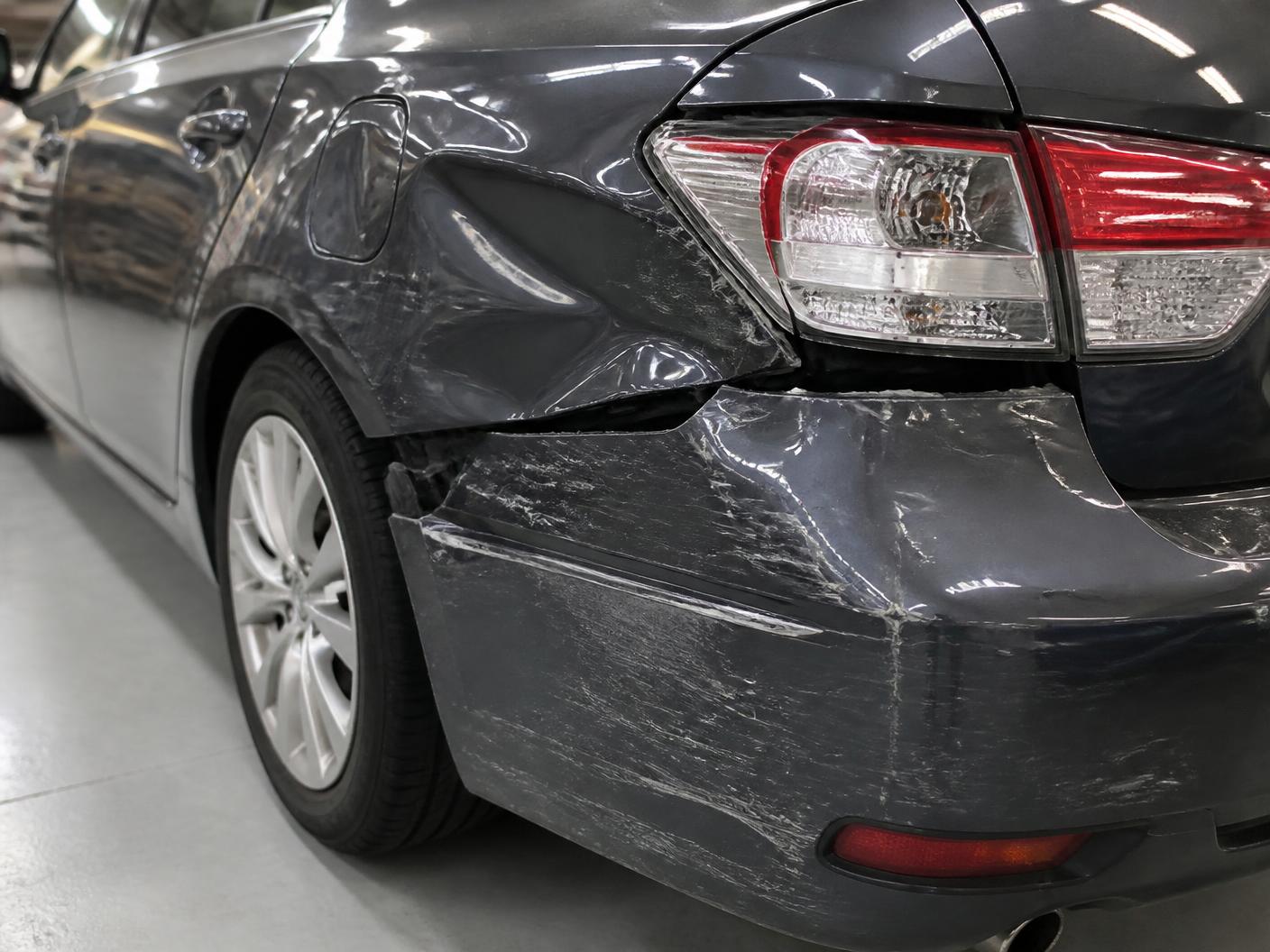 Charcoal gray sedan rear quarter panel with a deep dent and scraped paint before repair